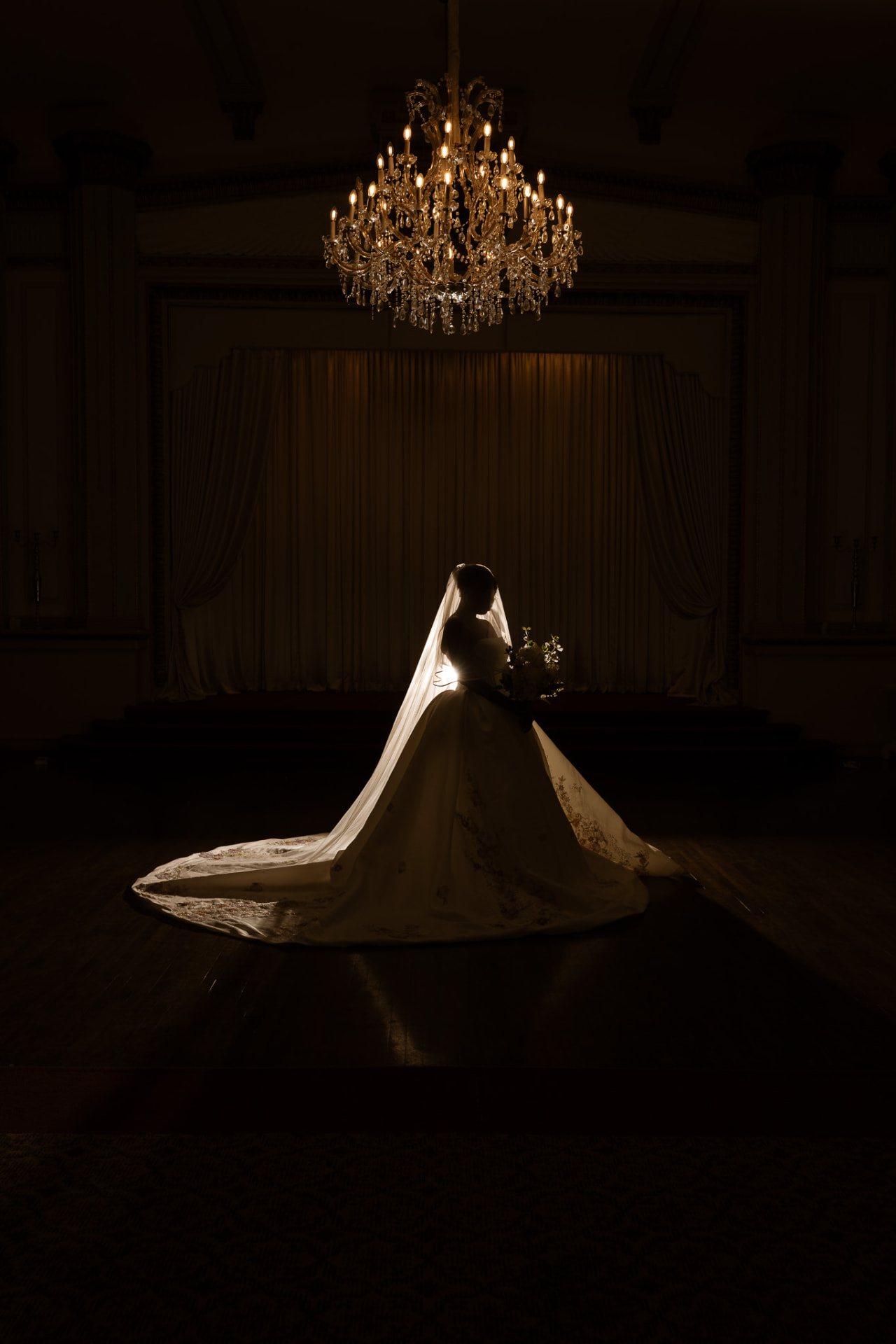 Bride silhouetted beneath a crystal chandelier in a candlelit ballroom